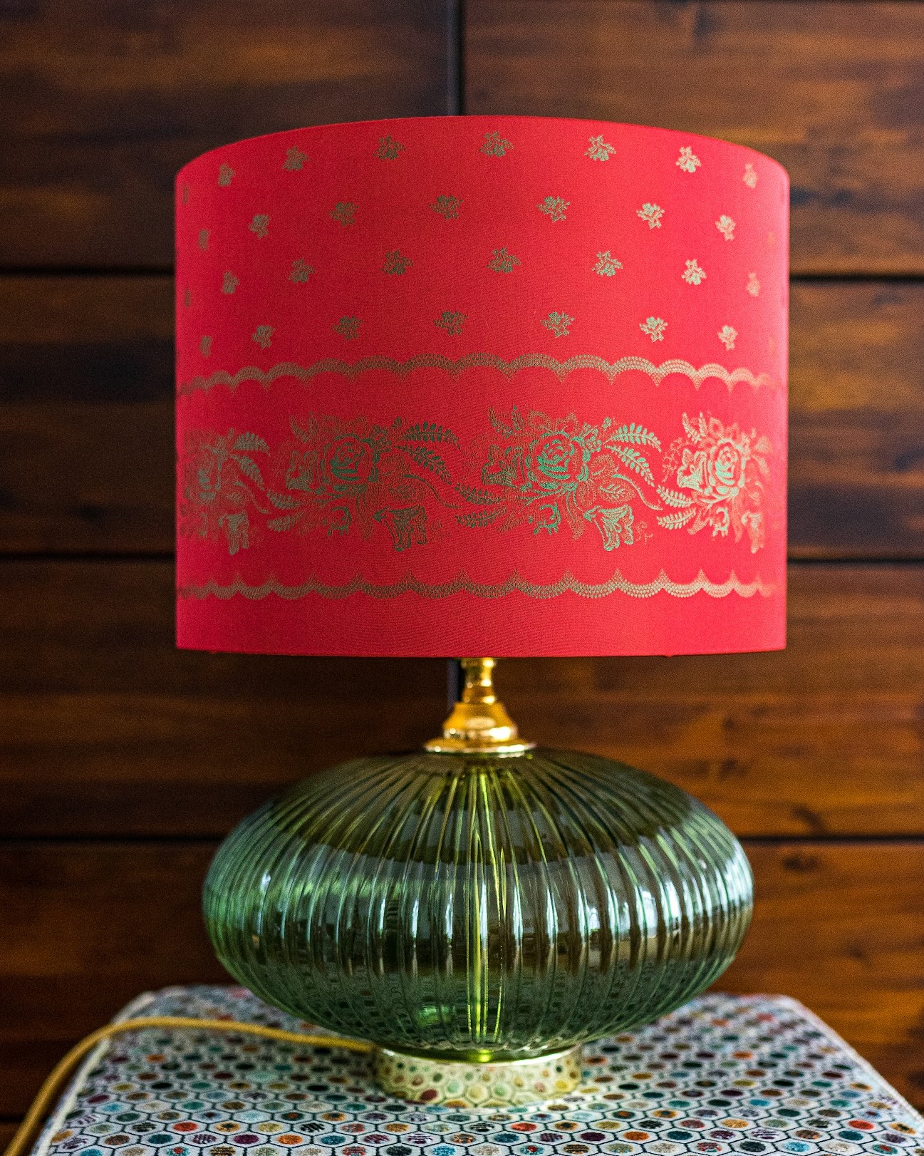 Lampe mit rotem Schirm und goldenem Muster auf grünem Glasfuß