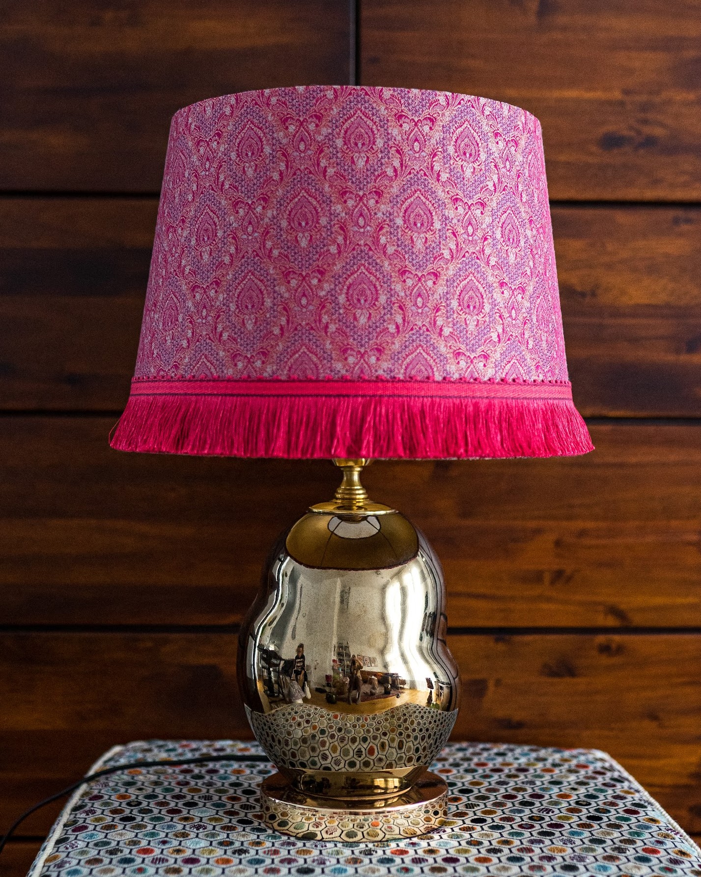 Lampe mit pinkem Fransenschirm auf goldenem Fuß